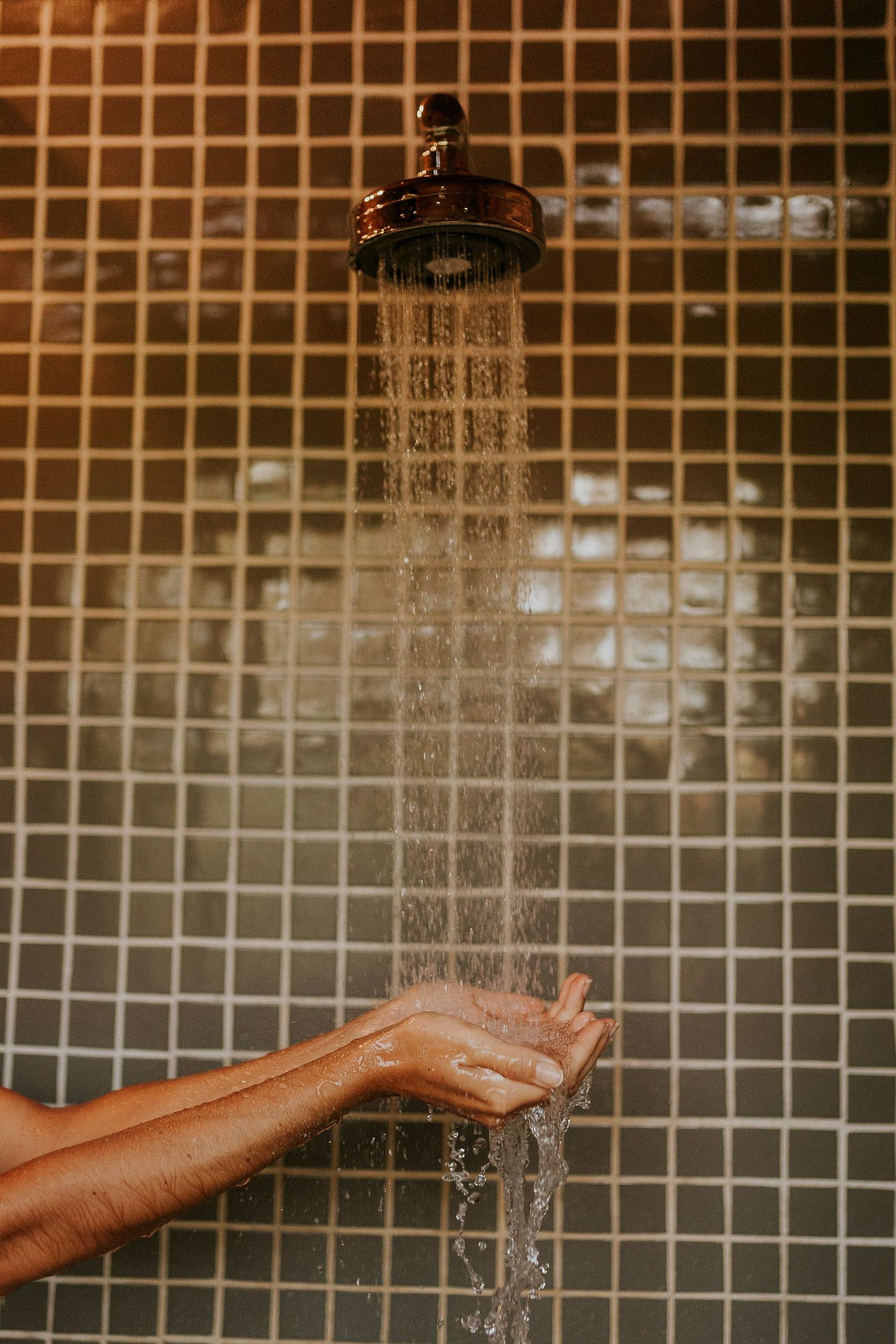 Una mano bajo un cabezal de ducha con agua corriendo.