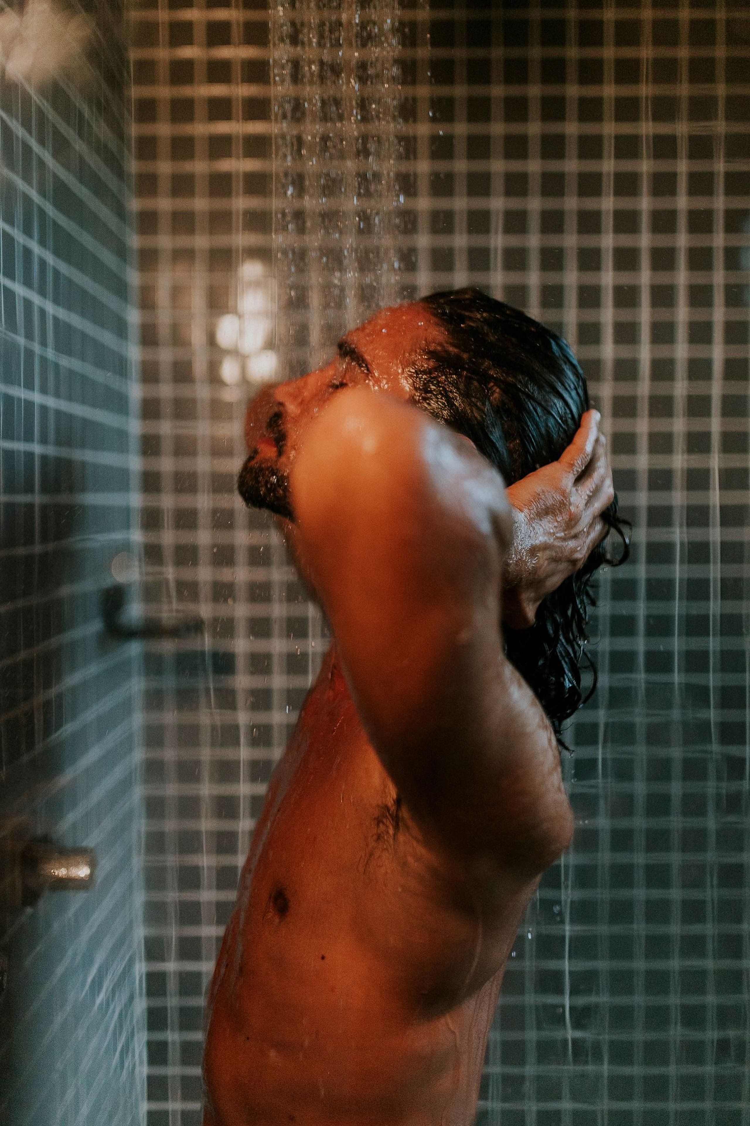 Une personne sous la douche, devant un mur carrelé.