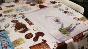 Une table à manger agrémentée d’un centre de table floral, une nappe blanche ornée de motifs imprimés et un verre d’eau.