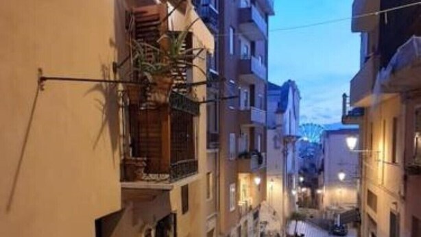 Une ruelle étroite pavée, bordée d’immeubles à plusieurs étages dotés de balcons et d’un éclairage extérieur.