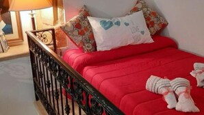 Un lit avec une literie rouge, un coussin à motifs floraux et un coussin en forme de cœur sur lequel est écrit « JE T’AIME ».