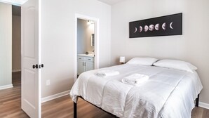 A bedroom with a bed, a nightstand, a wall-mounted artwork, and a door leading to a bathroom. - Winners Paradise Steps from Tiger Country - BC1033 (Baton Rouge)