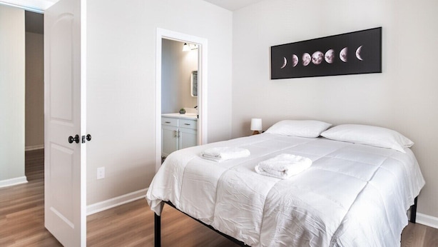 A bedroom with a bed, a nightstand, a wall-mounted artwork, and a door leading to a bathroom.