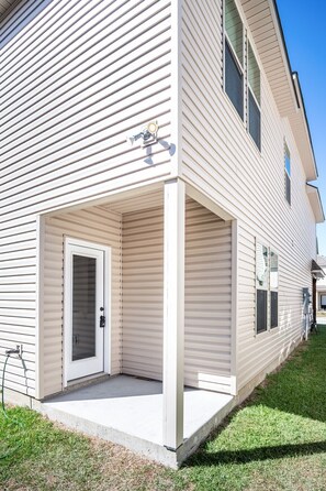 A two-story residential building with a covered front porch, a garage door, and a visible electrical box.