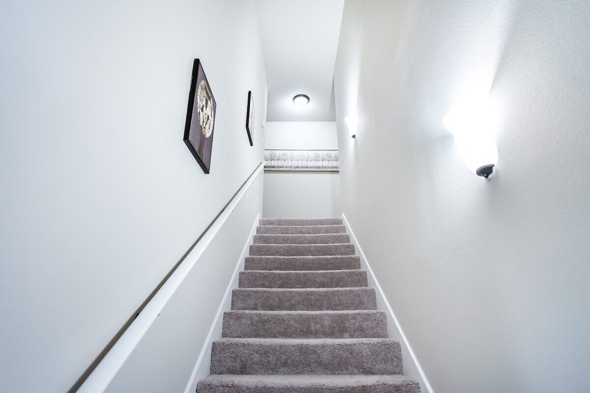 A carpeted staircase with a handrail, white walls, and a light fixture at the top.