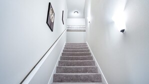 A carpeted staircase with a handrail, white walls, and a light fixture at the top.
