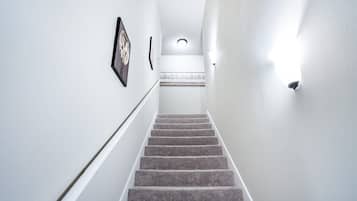 A carpeted staircase with a handrail, white walls, and a light fixture at the top.