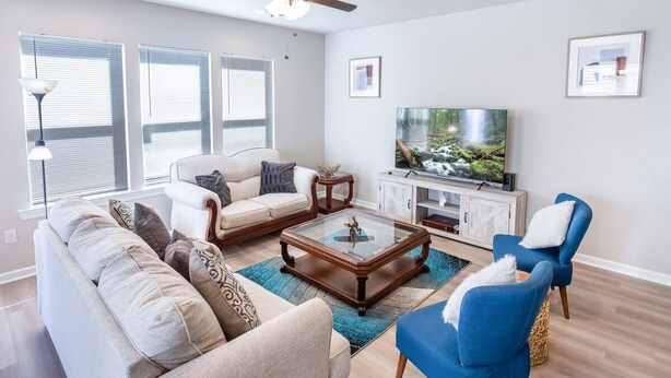 A living room with a sofa, armchairs, a coffee table, a television, and a cabinet. - Winners Paradise Steps from Tiger Country - BC1033 (Baton Rouge)