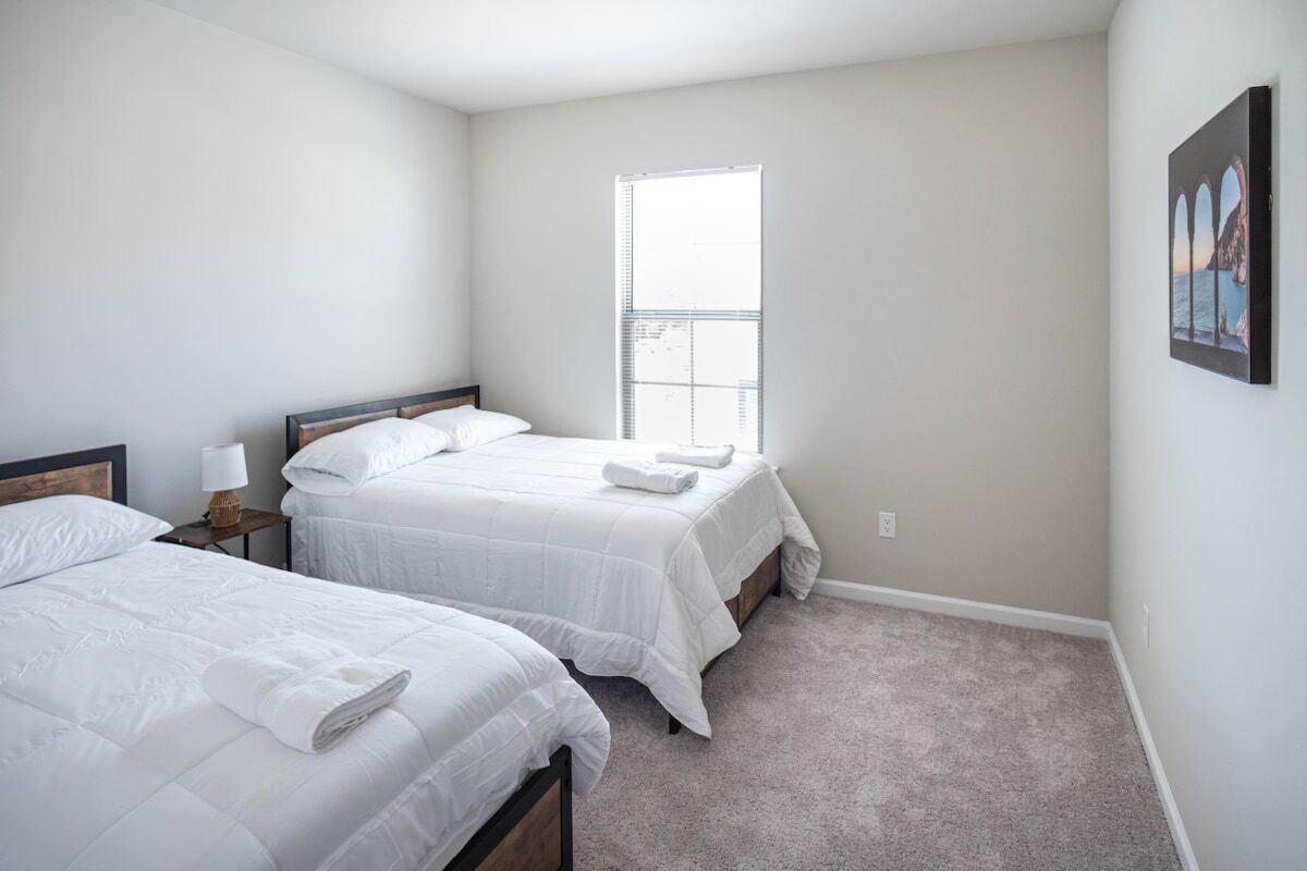 A bedroom with two beds, a window, and a painting on the wall.