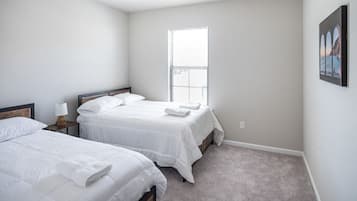A bedroom with two beds, a window, and a painting on the wall.