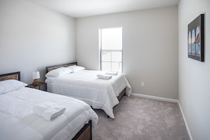A bedroom with two beds, a window, and a painting on the wall.
