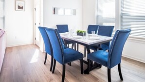 A dining area with a rectangular table set for four, surrounded by blue upholstered chairs with decorative stitching. - Winners Paradise Steps from Tiger Country - BC1033 (Baton Rouge)