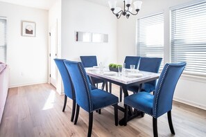 A dining area with a rectangular table set for four, surrounded by blue upholstered chairs with decorative stitching.