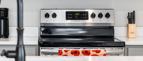 A kitchen with a stainless steel stove, a digital clock, and a coffee maker.