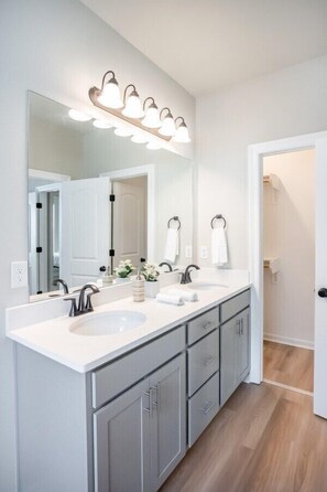 A bathroom with a double sink vanity, a large mirror, and a lighted vanity area.