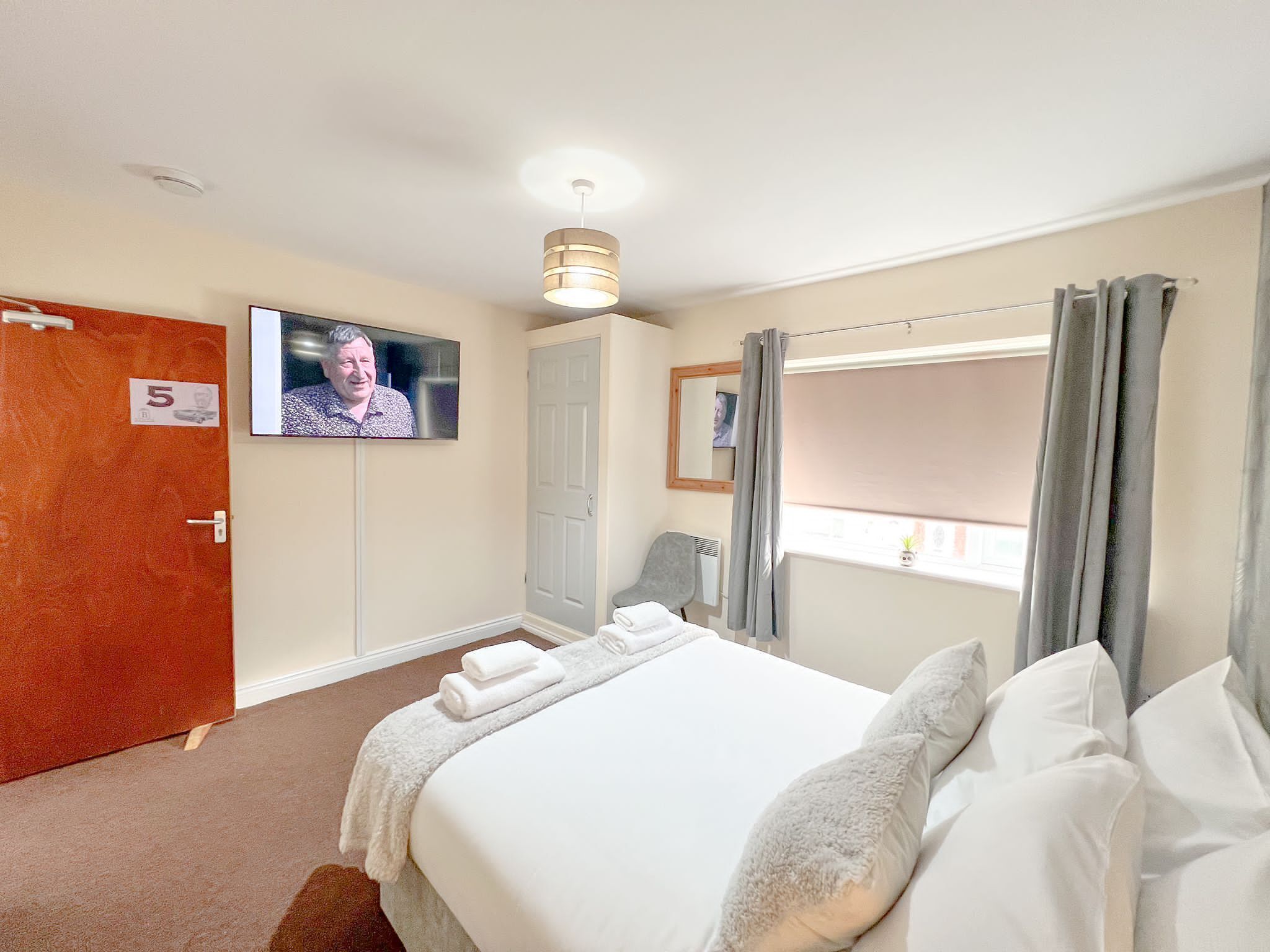 Una habitación de hotel con cama, televisión, puerta con número y ventana con cortinas.