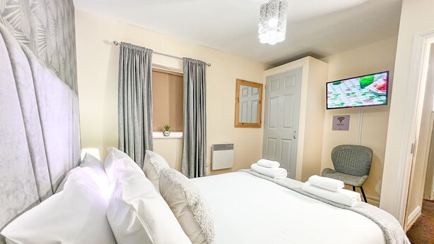 Une chambre d’hôtel avec un lit, une télévision, une chaise et une fenêtre avec des rideaux.