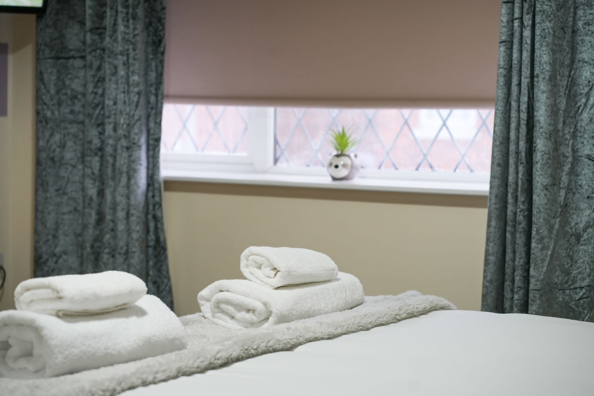 Een net opgemaakt bed met opgerolde witte handdoeken en een zachte, witte deken.