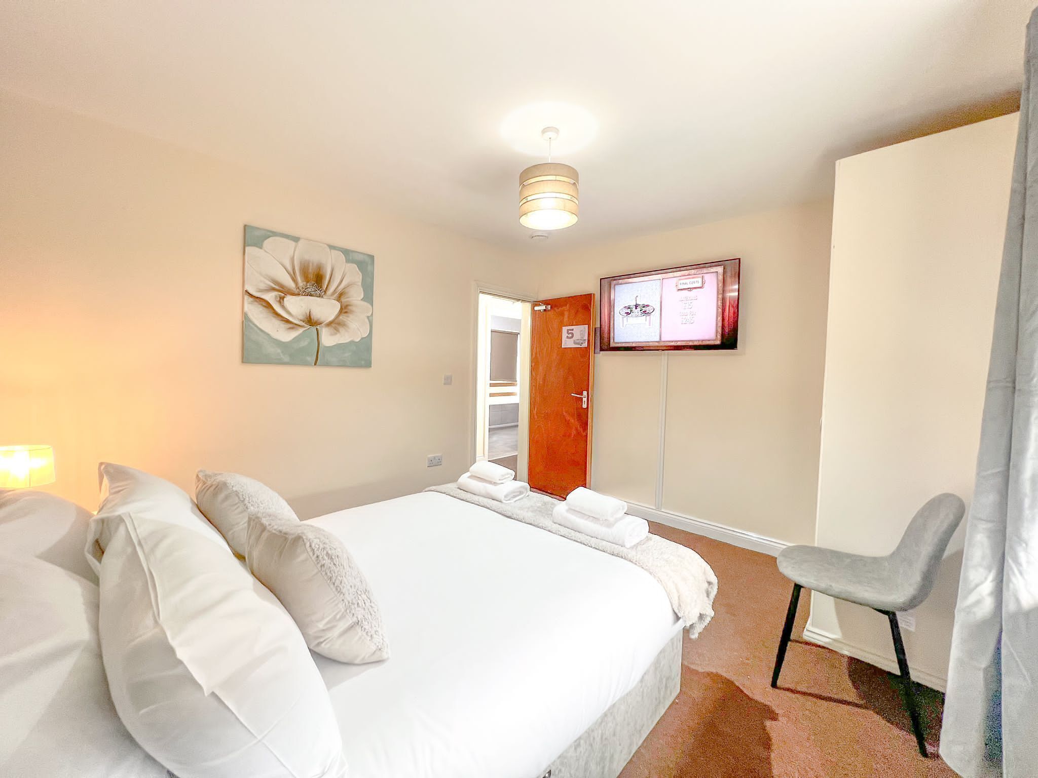 Una camera d'albergo con un letto, una sedia, una televisione e una porta con un numero.