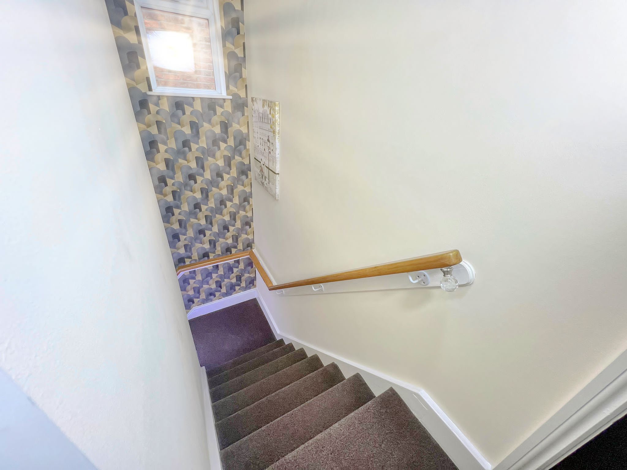 Una escalera con escalones alfombrados, barandilla de madera y pared con diseño.