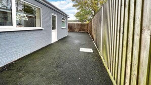 Un petit jardin à l’arrière de la maison, avec un mur en briques grises, une clôture en bois et une zone pavée.