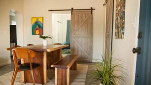 A dining area with a wooden table and chairs, a bench, a potted plant, and a sliding barn door. - NEW Modern 1940s Adobe - Downtown, Historic (Tucson)