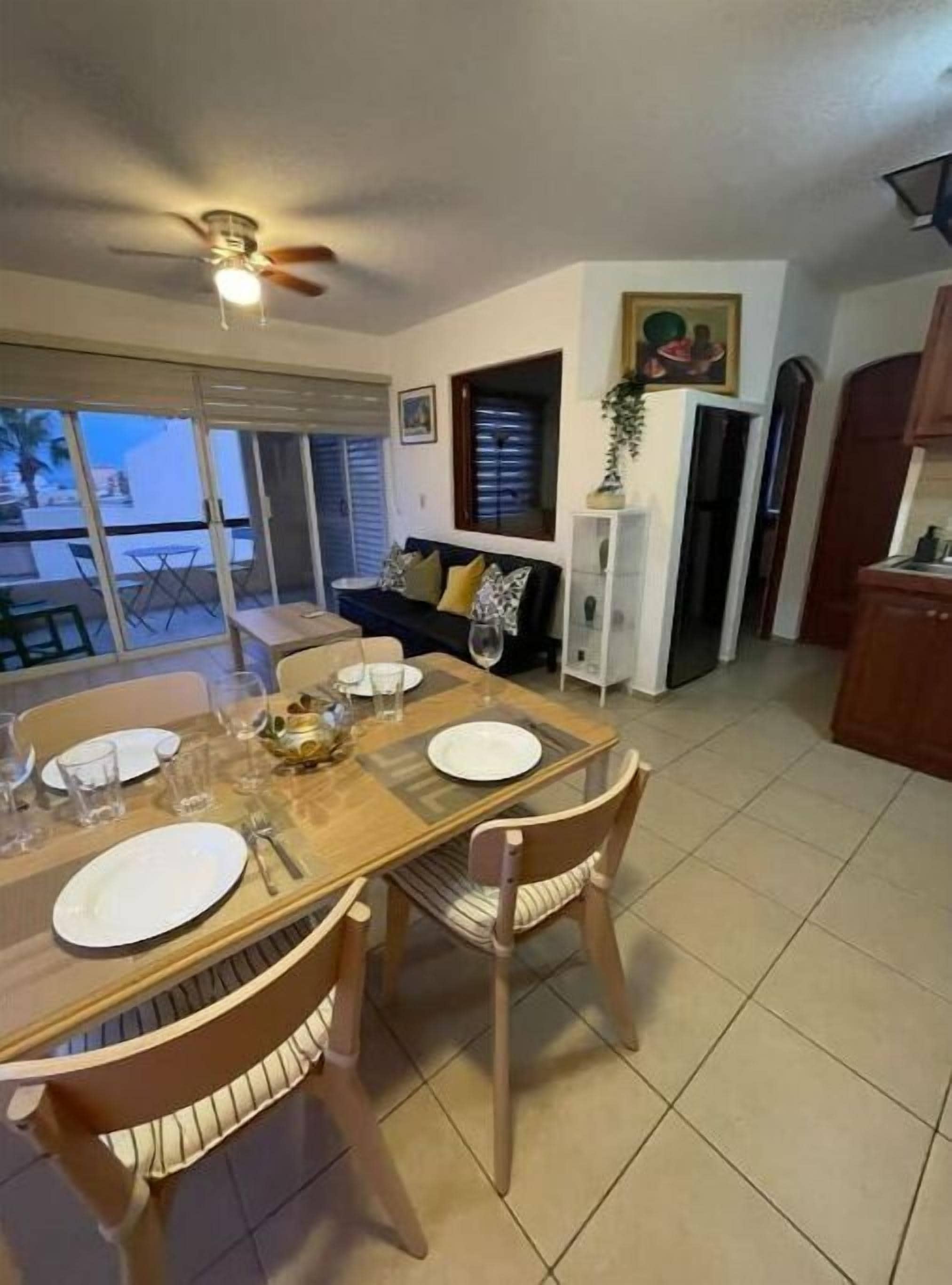 A dining area with a table set for four, a ceiling fan, and a view through the glass doors.