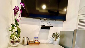 A kitchen with white cabinets, a stainless steel refrigerator, a flat-screen TV mounted above the counter, and a potted orchid on the counter. - Pride Villa Cambodia (Phnom Penh)