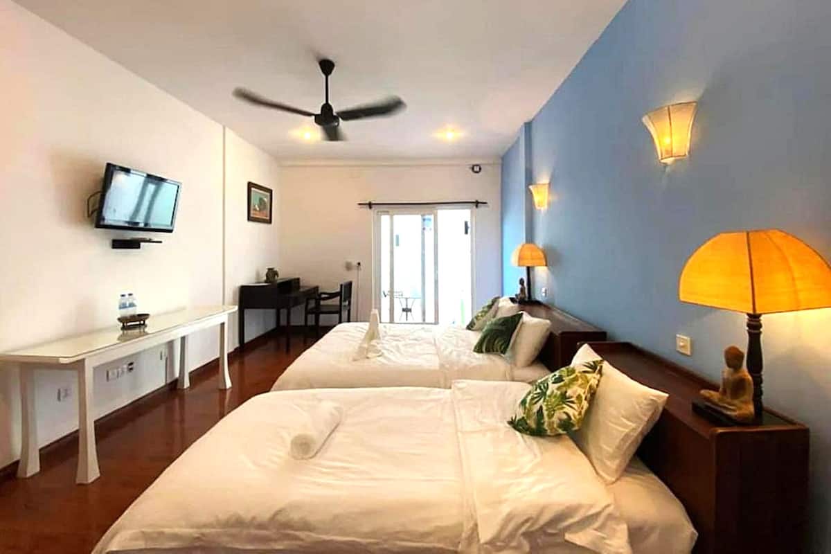A hotel room with two beds, a desk, a television, a ceiling fan, and a view of the outside.