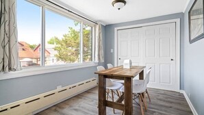 A room with a wooden table and chairs, a white door, and a window with a view of houses and trees. - The Norwood Nook – Walkable Stay Near O’Hare & Metra! (Chicago)