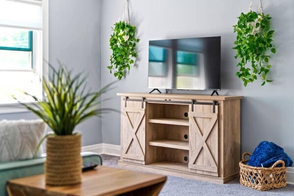 Una habitación con una televisión sobre un mueble de madera, una planta sobre una mesa y una cesta en el suelo.