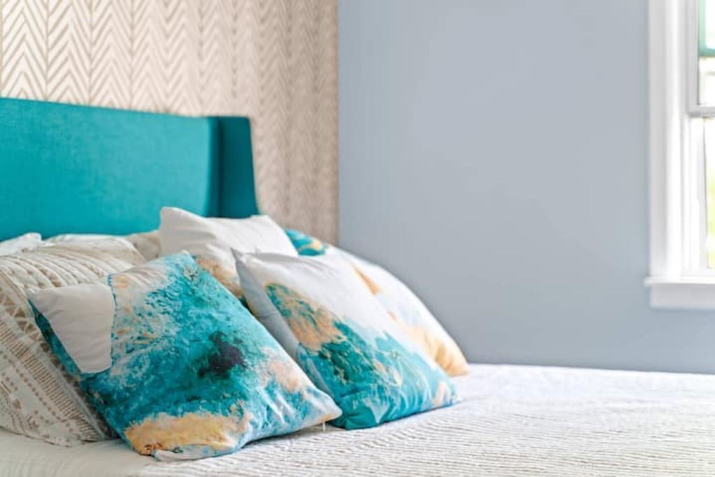A bed with a teal headboard, white bedding, and blue and white patterned pillows.