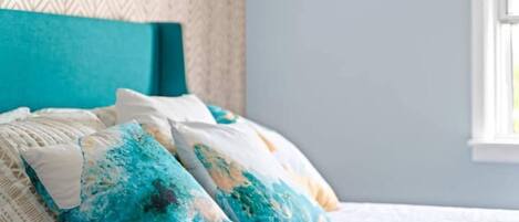 A bed with a teal headboard, white bedding, and blue and white patterned pillows.