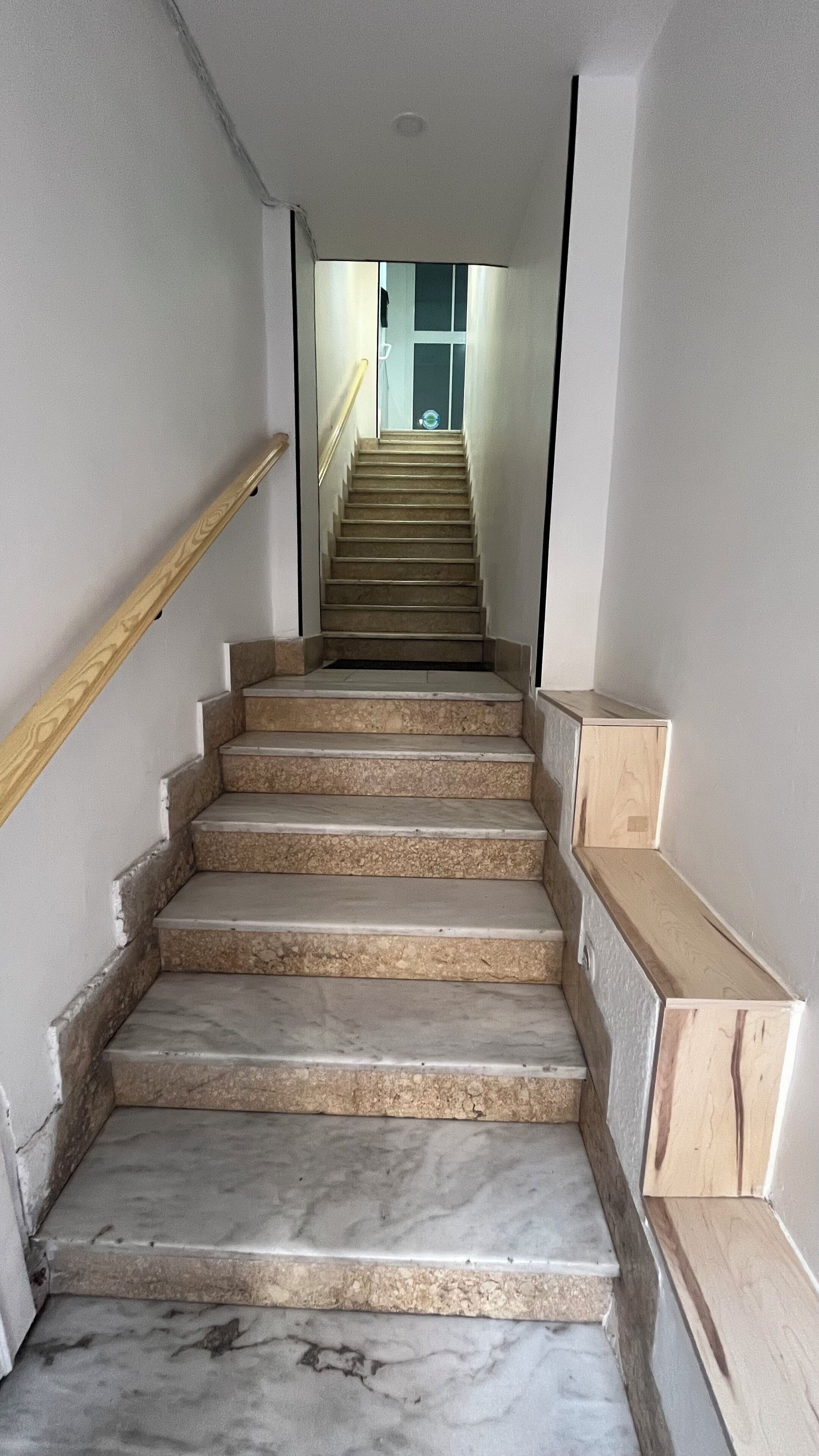 Una escalera con escalones de mármol y barandillas de madera, que conduce a una puerta en la parte superior.