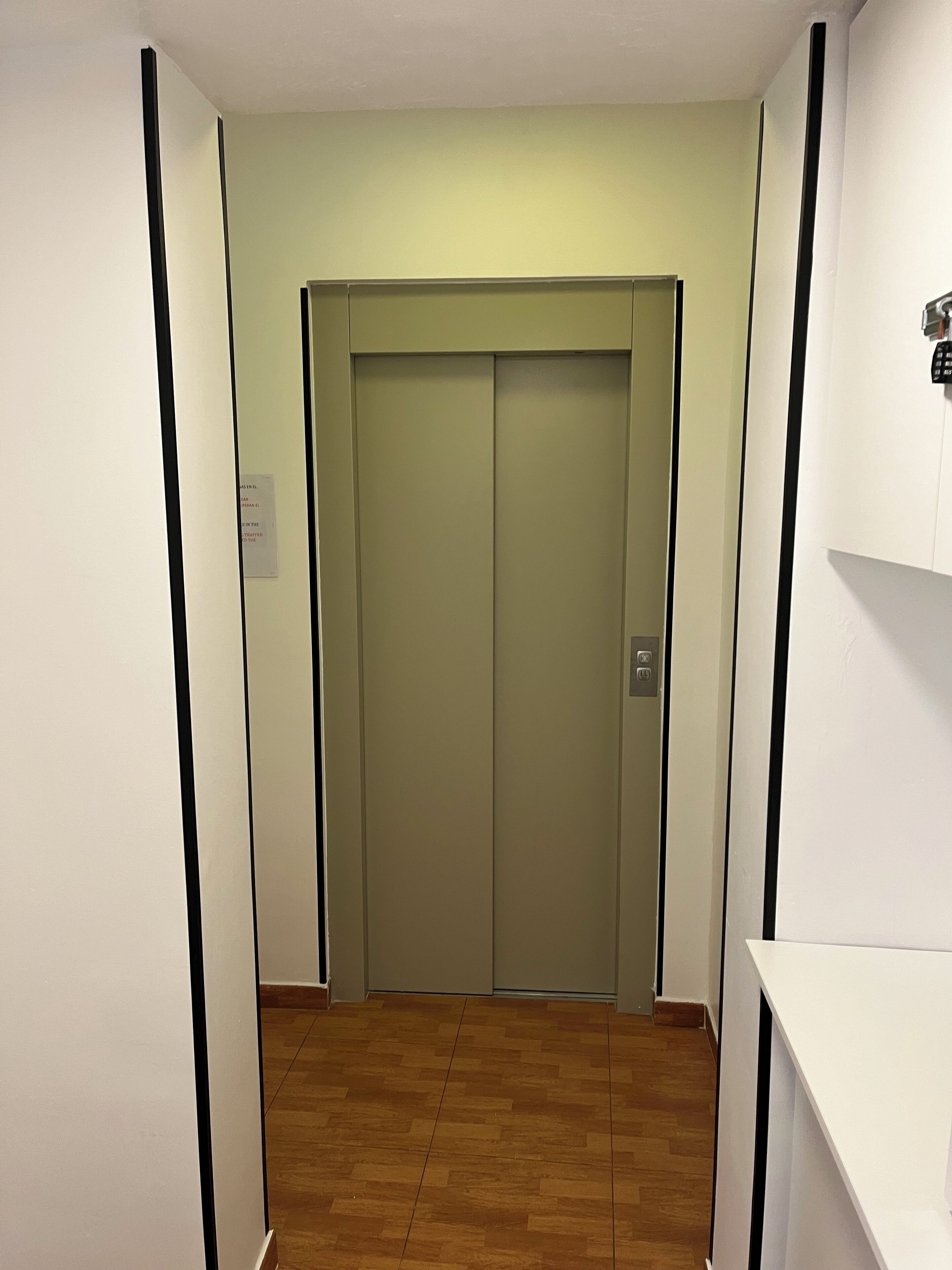 Un pasillo con piso de madera que lleva a una puerta cerrada de ascensor.