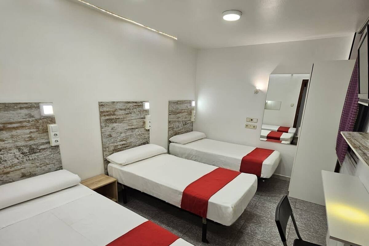Una habitación de hotel con tres camas individuales, un escritorio, una silla y un espejo.