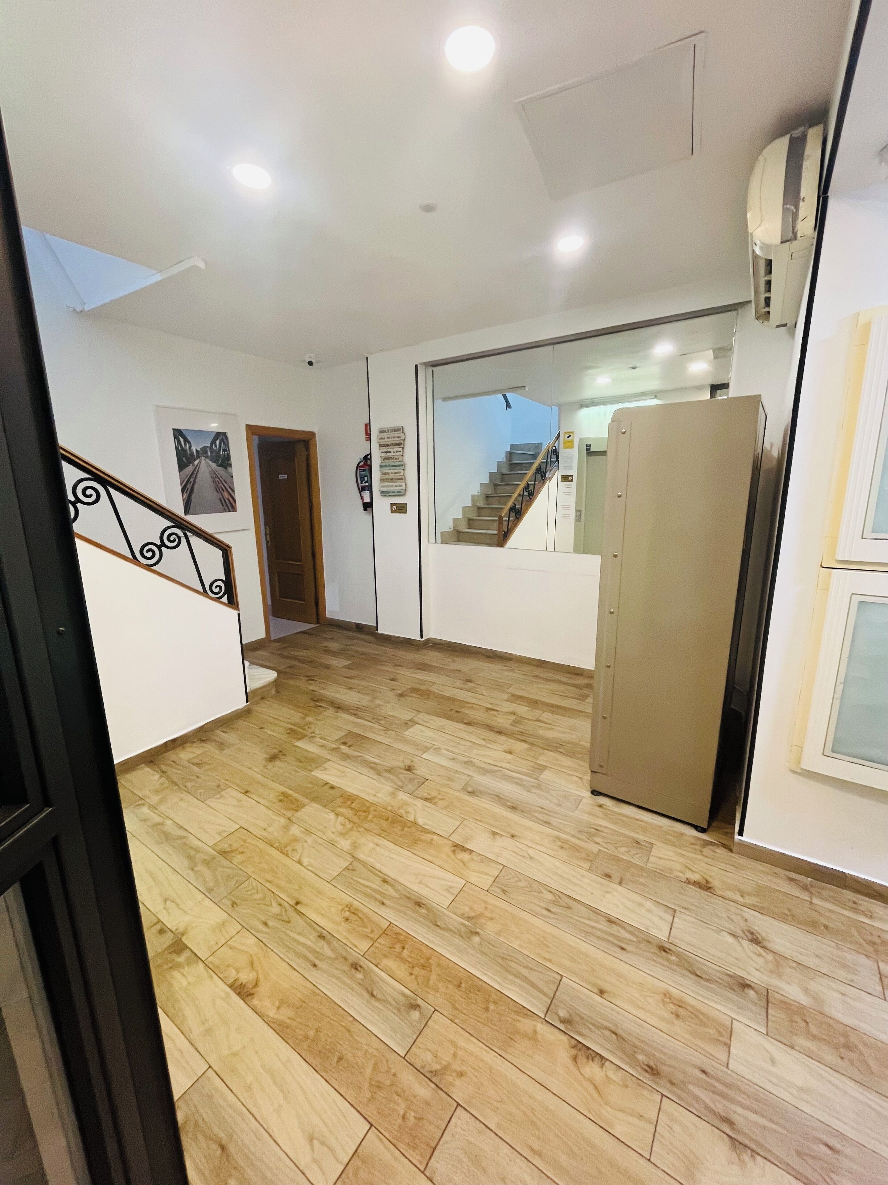 A hallway with wooden flooring, a staircase, a door, and a refrigerator.
