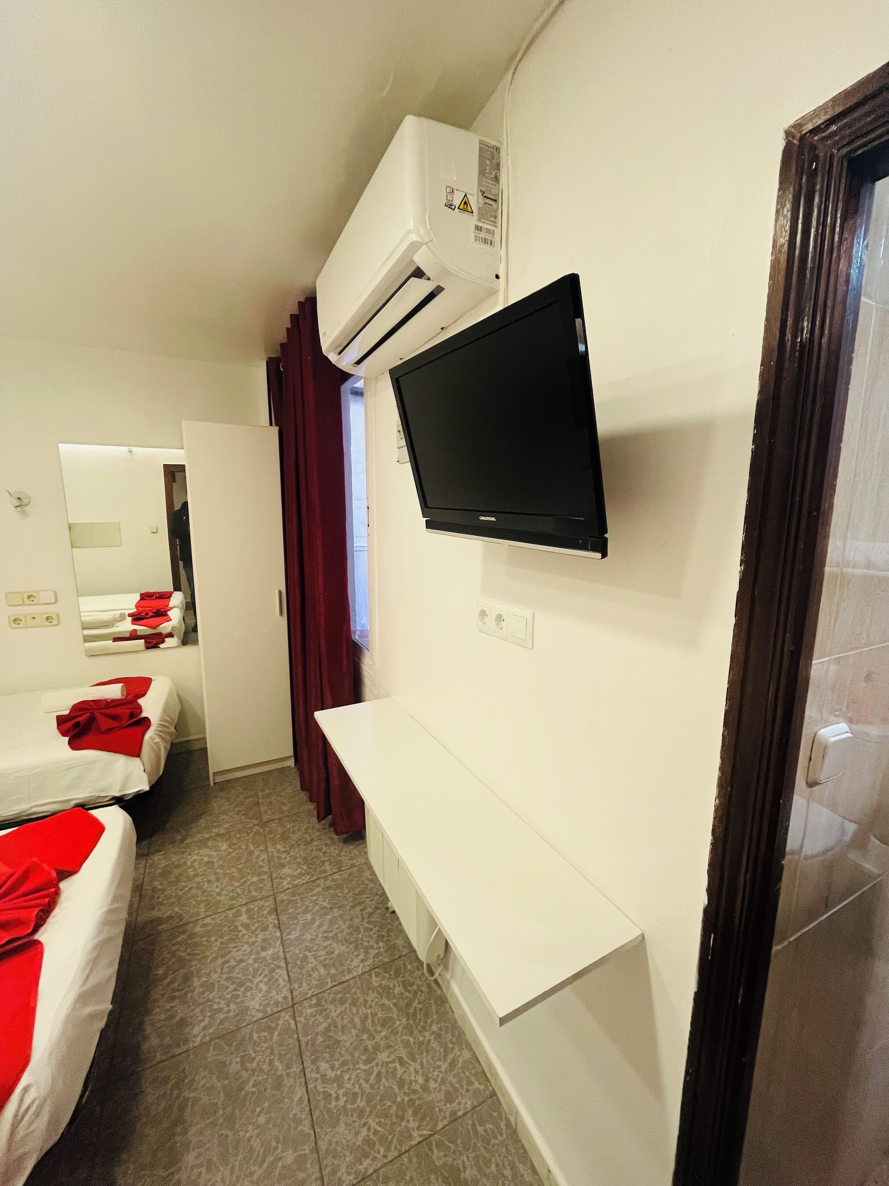 Hotelkamer met twee bedden, een aan de muur bevestigde televisie, een airconditioner en een raam met gordijnen.