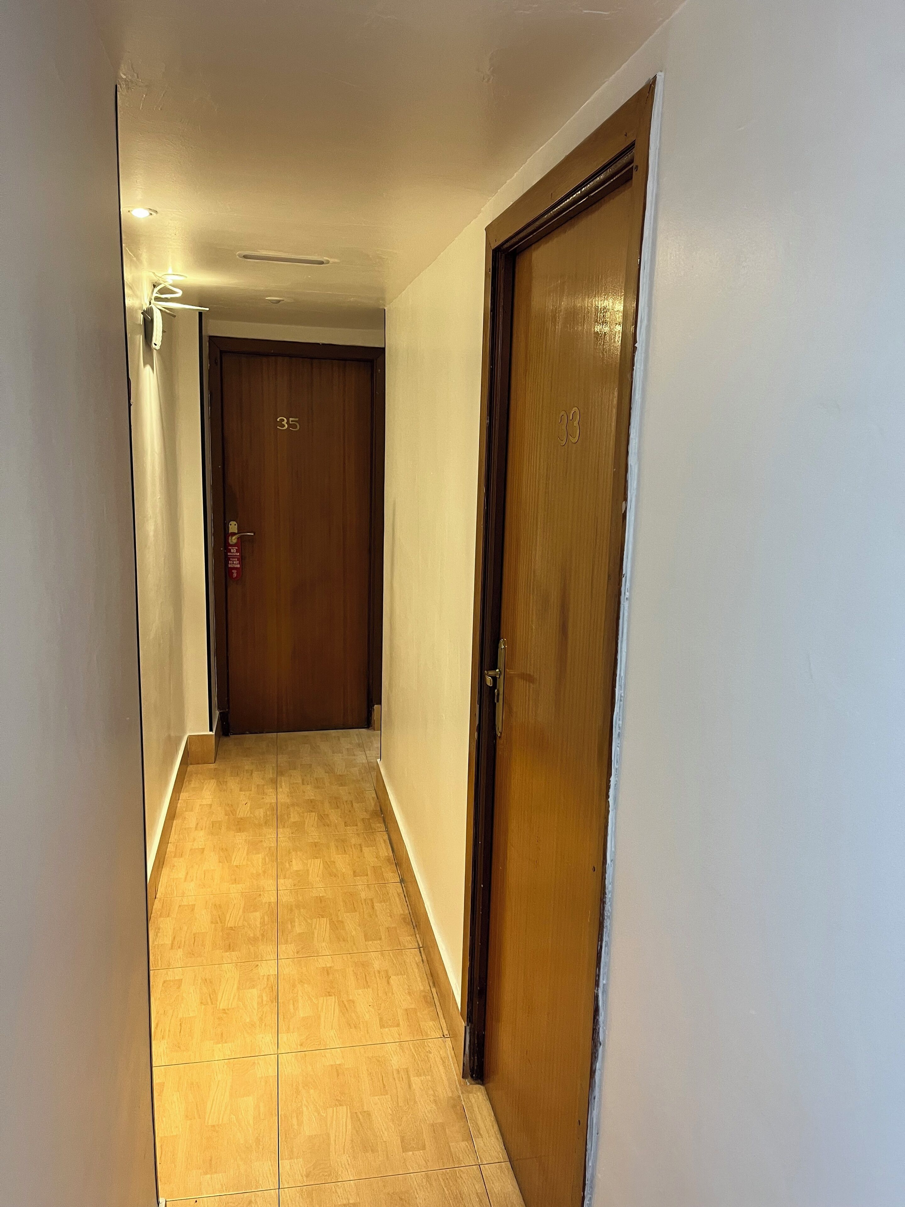 A narrow hallway with wooden doors, a tiled floor, and a ceiling with recessed lighting.