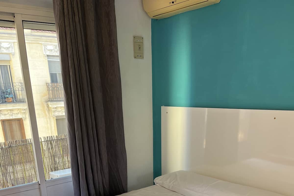 Habitación con cama individual, colchón blanco, manta roja y pared de acento color aguamarina.