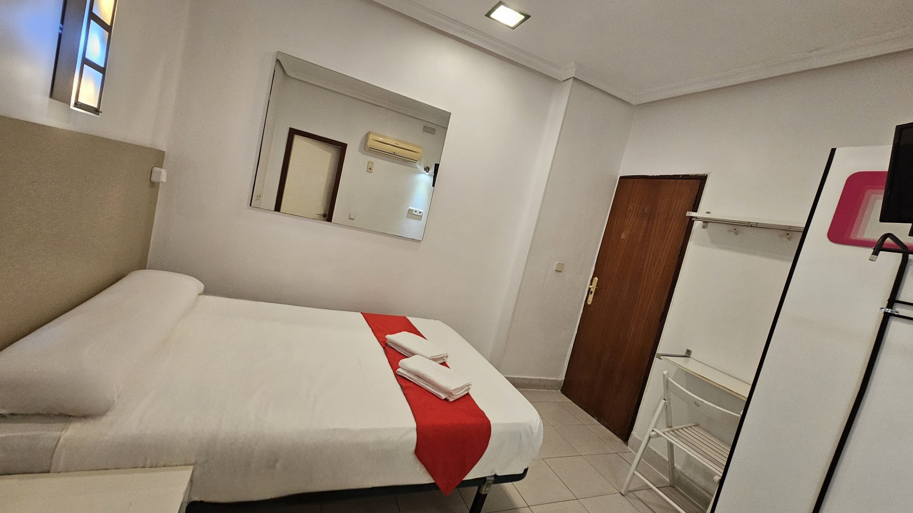 Une chambre d’hôtel équipée d’un lit, d’un miroir, d’un climatiseur, d’une armoire et d’un téléviseur.