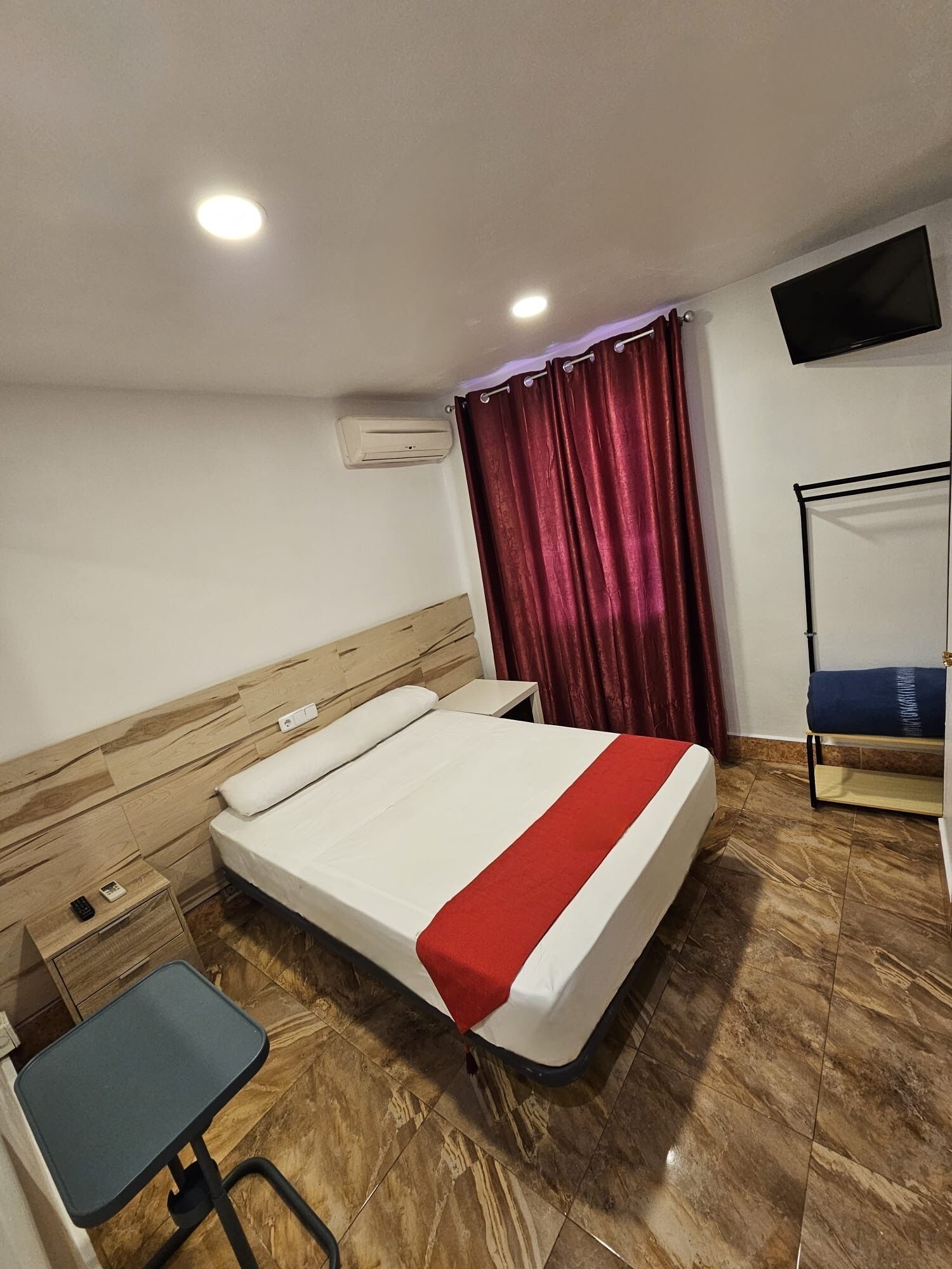 A hotel room with a bed, a desk, a chair, a TV on the wall, and a window with curtains.