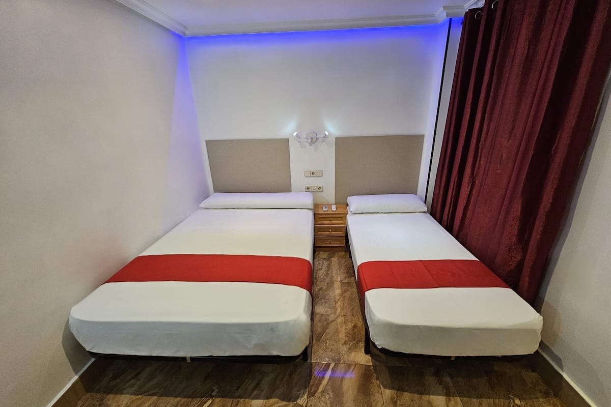 Habitación doble con dos camas, suelo de madera y techo iluminado en azul.