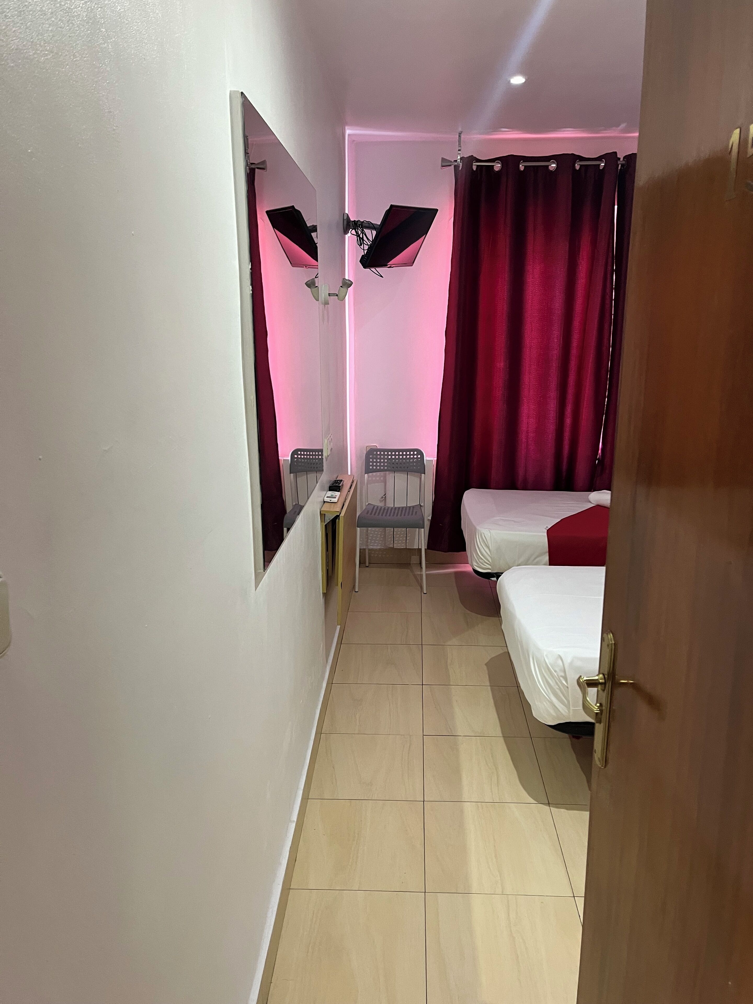 Quarto de hotel com uma cama, uma cadeira, uma escrivaninha e um espelho.