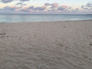 Una playa arenosa con huellas y un mar tranquilo bajo un cielo nublado.