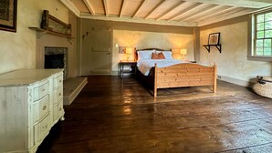 Een slaapkamer met een houten bed, een dressoir, een open haard en een raam.