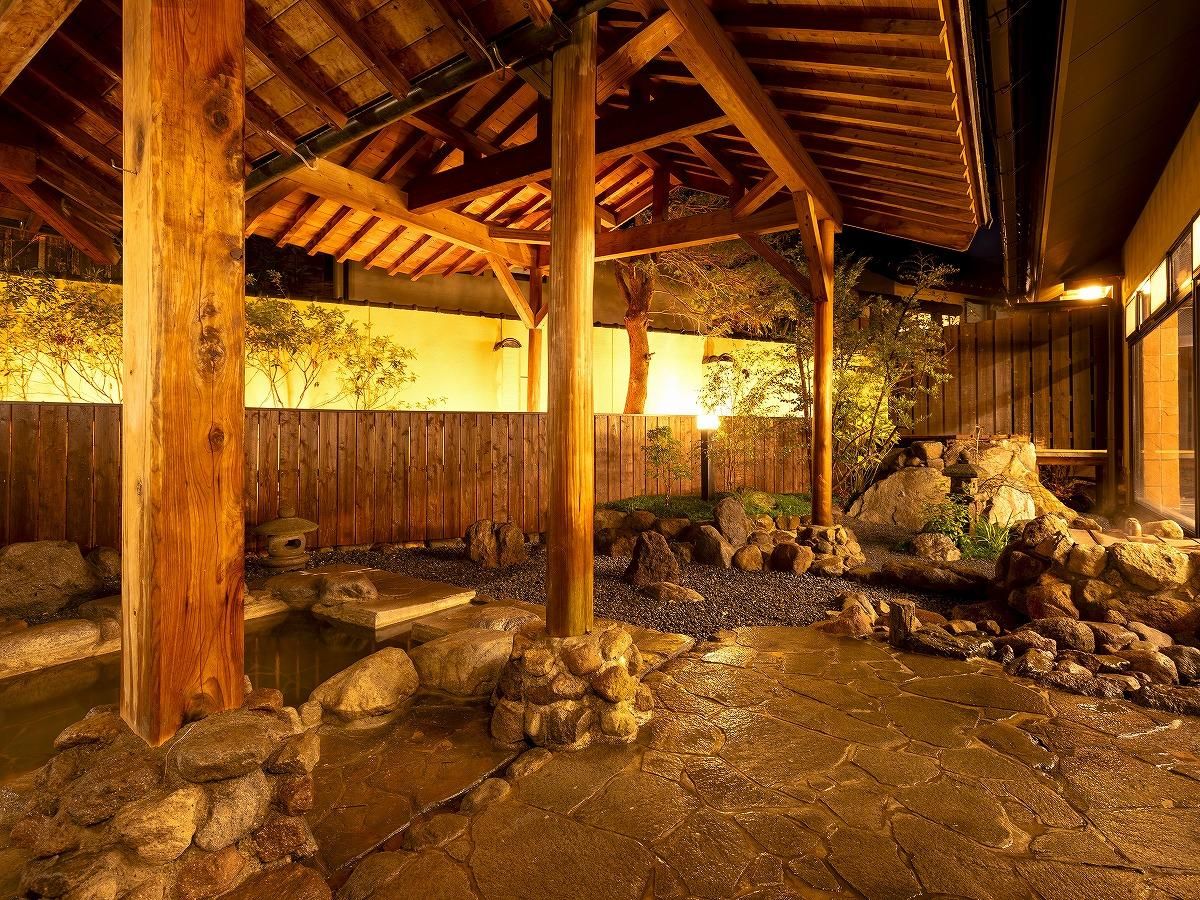 Un onsen japonés tradicional con vigas de madera, un baño de piedra y una cerca de madera.