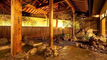 Un onsen japonés tradicional con vigas de madera, un baño de piedra y una cerca de madera.