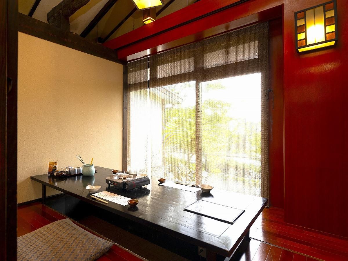 Una habitación japonesa tradicional con suelo de tatami, una mesa baja con juego de té y un ventanal con vistas a zonas verdes.