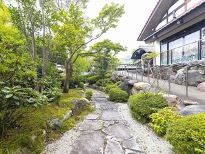 A traditional Japanese garden with a stone pathway, various shrubs, and a building with a tiled roof. - Nagomi no Yado Mutsuki (Beppu)